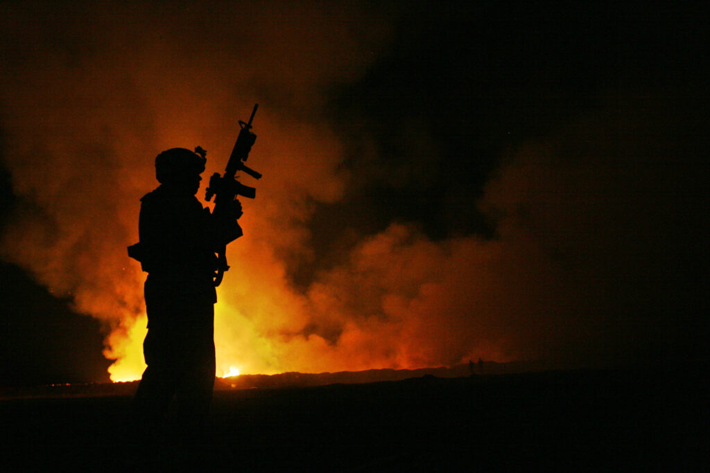 Sgt. Robert B. Brown from Fayetteville, N.C. with Regimental Combat Team 6, Combat Camera Unit watches over the civilian Fire Fighters at the burn pit as smoke and flames rise into the night sky behind him on May 25th, 2007. Camp Fallujah has its own civilian run Fire Department to assist the Marines and Soldiers during a fire or emergency. Regimental Combat Team 6 is deployed with Multi National Forces-West in support of Operation Iraqi Freedom in the Al Anbar Province of Iraq to develop Iraqi Security Forces, facilitate the development of official rule of law through democratic reforms, and continue the development of a market based economy centered on Iraqi reconstruction. (Official USMC photograph by Cpl. Samuel D. Corum)(RELEASED)(RELEASED)